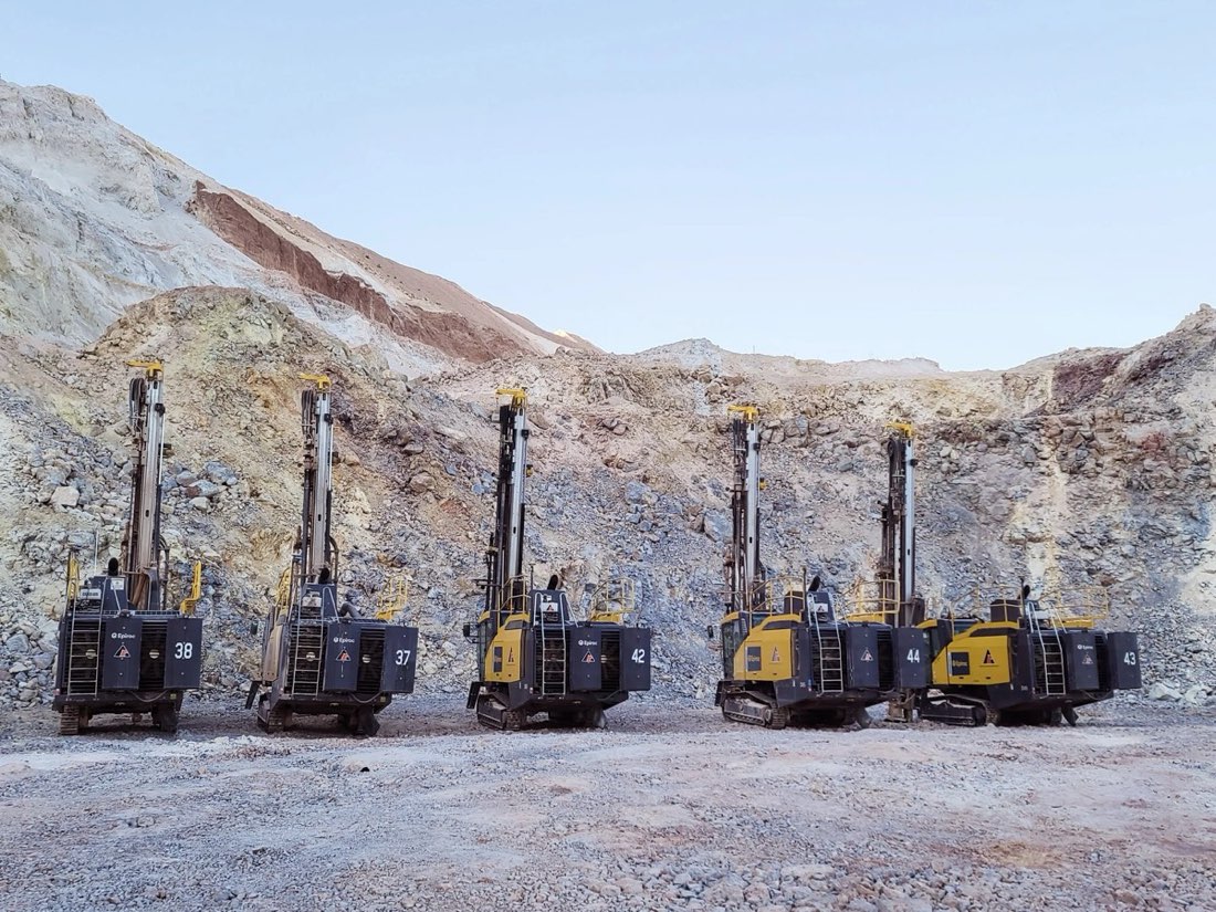 A row of five tracked Epiroc drill rigs parked against a quarry wall